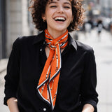 A woman wearing Orange silk scarf with equestrian belt and buckle stripe pattern and navy blue border, styled tied over a book.