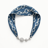 A blue silk scarf with a silver chain link pattern and silver pavé-embellished spherical charms, displayed on a clean white background.