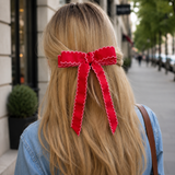 Person with long blonde hair wearing a large red bow, walking on a city street.
