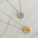 Two necklaces with circular pendants featuring crosses on a marble surface.