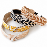 Four woven fabric headbands with braided leaf patterns, arranged overlapping on a white background. The headbands feature color combinations of beige and brown, black and beige, yellow and beige, and light blue and beige.