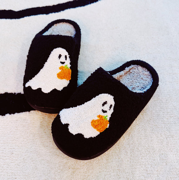 Black cozy slippers featuring a white ghost with a pumpkin detail, offering a playful and spooky seasonal touch.