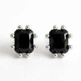 A pair of black gemstone stud earrings featuring faceted rectangular stones set in silver-toned prong settings, offering a bold and refined statement look.