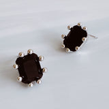 A pair of black gemstone stud earrings featuring faceted rectangular stones set in silver-toned prong settings, offering a bold and refined statement look.