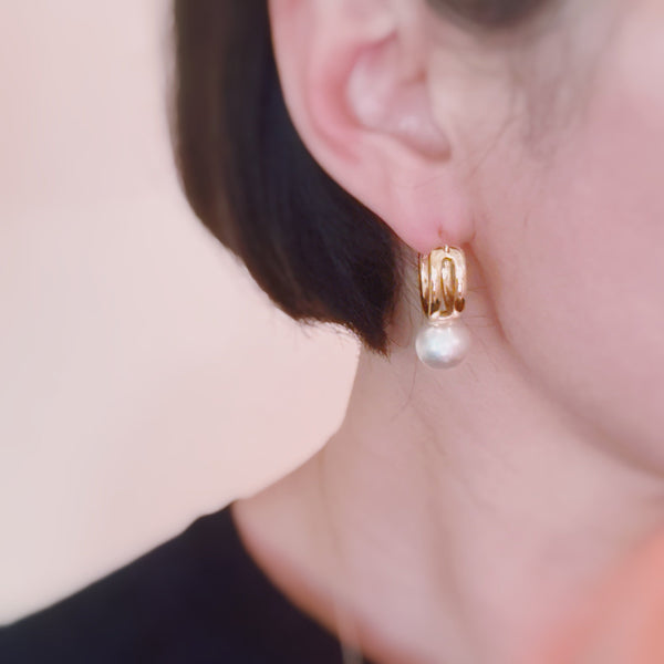 Elegant gold-tone hoop earrings featuring a single dangling white pearl, combining classic charm with a modern drop design.