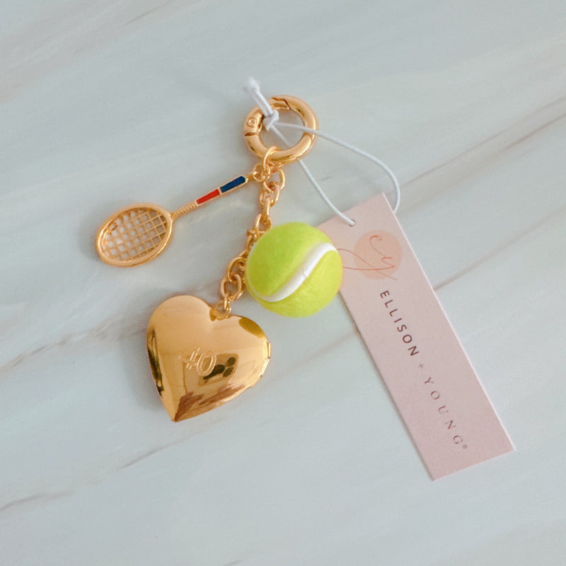 Gold heart-shaped keychain with tennis racket and ball charm on a light background