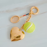 Gold charm with tennis racket and ball on a light gray background