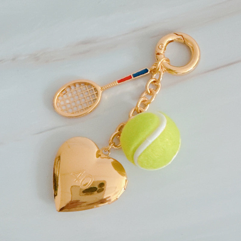 Gold charm with tennis racket and ball on a light gray background