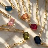 Gold chain necklaces with colorful gemstones on a marble surface