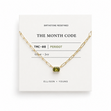 Gold necklace with a green gemstone on a white card displaying 'The Month Code' branding.
