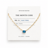 Gold necklace with blue gemstone on a white card displaying 'The Month Code' branding.