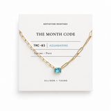 Gold necklace with a blue gemstone on a white card displaying 'The Month Code' branding.