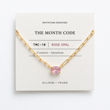 Gold necklace with a pink gemstone on a 'The Month Code' card.