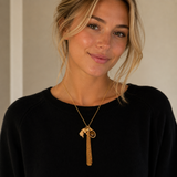 Woman wearing a black top and gold necklace with a tassel against a neutral background