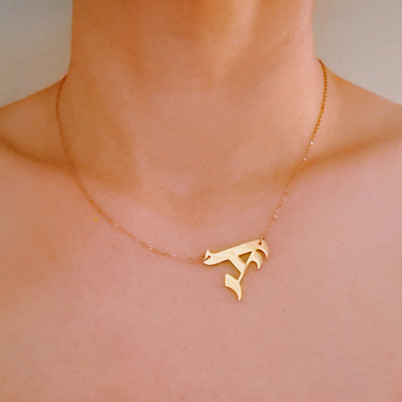 Gold-tone chain necklace featuring a bold Gothic-style initial charm that hangs asymmetrically to the side, adding a vintage-inspired yet edgy detail to your layered look.
