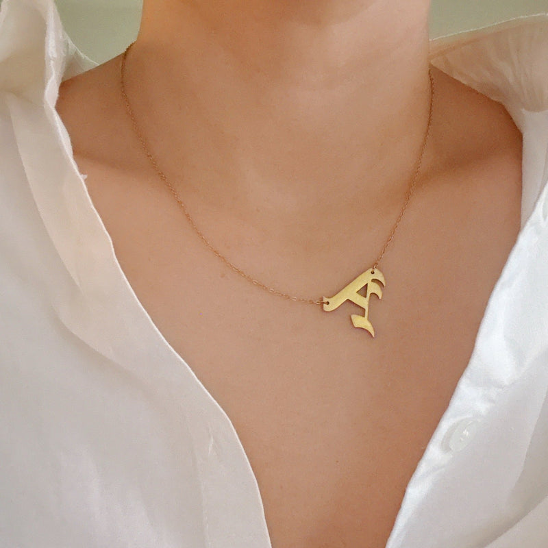 Gold-tone chain necklace featuring a bold Gothic-style initial charm that hangs asymmetrically to the side, adding a vintage-inspired yet edgy detail to your layered look.