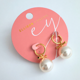 Sleek gold-tone toggle bar earrings featuring a lustrous pearl drop, blending modern structure with timeless charm for a refined, fashion-forward statement.