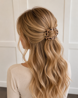 Woman with long, wavy blonde hair wearing a leopard print hair clip against a white paneled wall.