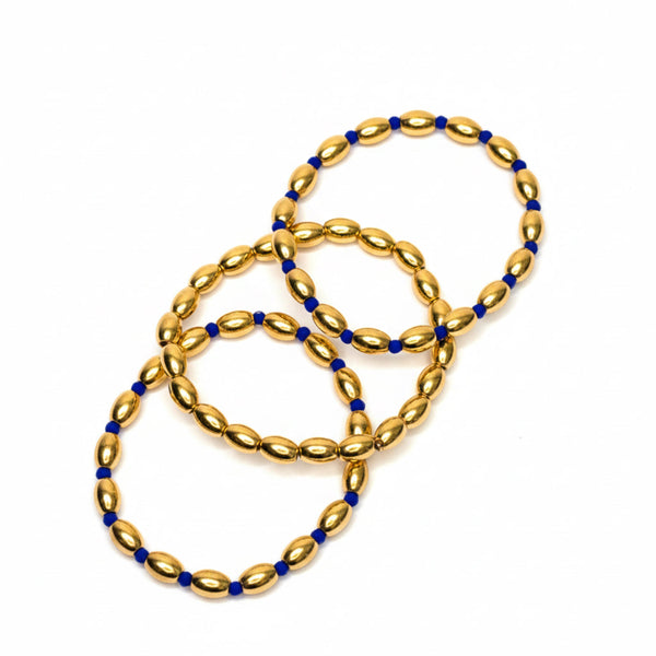 Three sets of glossy gold-tone oval bead stretch bracelets, each accented with different colored spacer beads in red, navy, or black; each set includes three coordinating bracelets.
