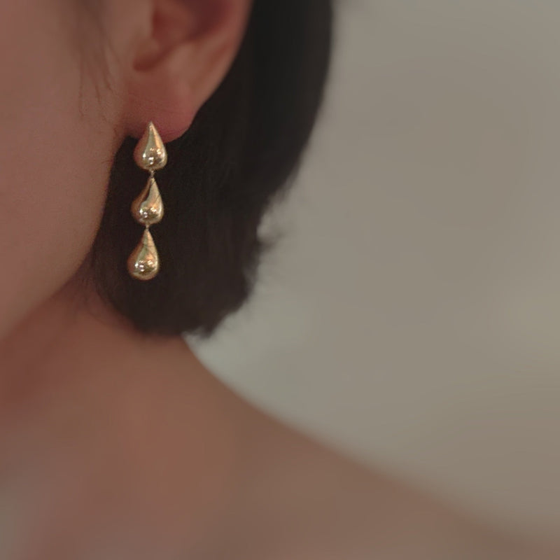 Gold-tone earrings featuring three cascading teardrop shapes in a tiered design, creating an elegant and fluid silhouette.