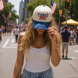A woman wearing Cream baseball cap featuring “USA 250th Anniversary” embroidery with red and blue firework accents and a blue star-print brim for a patriotic Americana look. On the street.