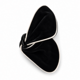 A pair of black velvet slippers with white trim, arranged in a knotted bow-like shape on a clean white background.