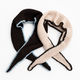 Two knitted awareness ribbons, one dark brown with a light blue edge and one cream with a black edge, displayed on a white background.