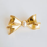 Elegant bow-shaped brooch pin with a vintage-inspired design, featuring a pearl and textured gold-tone metal—perfect for adding charm to jackets, scarves, or bags.