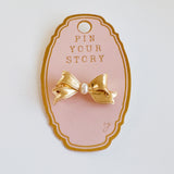 Elegant bow-shaped brooch pin with a vintage-inspired design, featuring a pearl and textured gold-tone metal—perfect for adding charm to jackets, scarves, or bags.