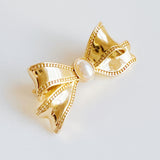 Elegant bow-shaped brooch pin with a vintage-inspired design, featuring a pearl and textured gold-tone metal—perfect for adding charm to jackets, scarves, or bags.