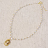 Vintage-style necklace featuring a classic cameo pendant framed in gold-tone detailing, suspended from a pearl-accented chain for an elegant and timeless look.