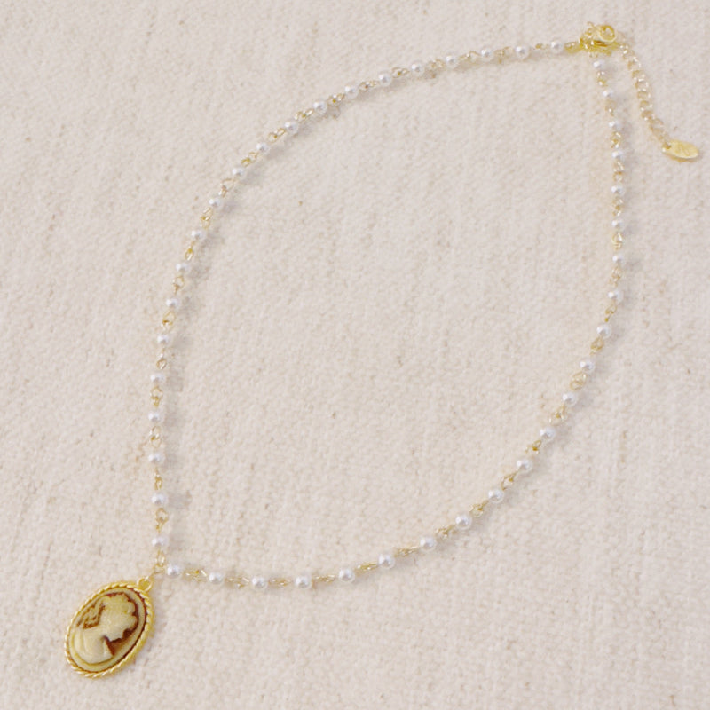Vintage-style necklace featuring a classic cameo pendant framed in gold-tone detailing, suspended from a pearl-accented chain for an elegant and timeless look.