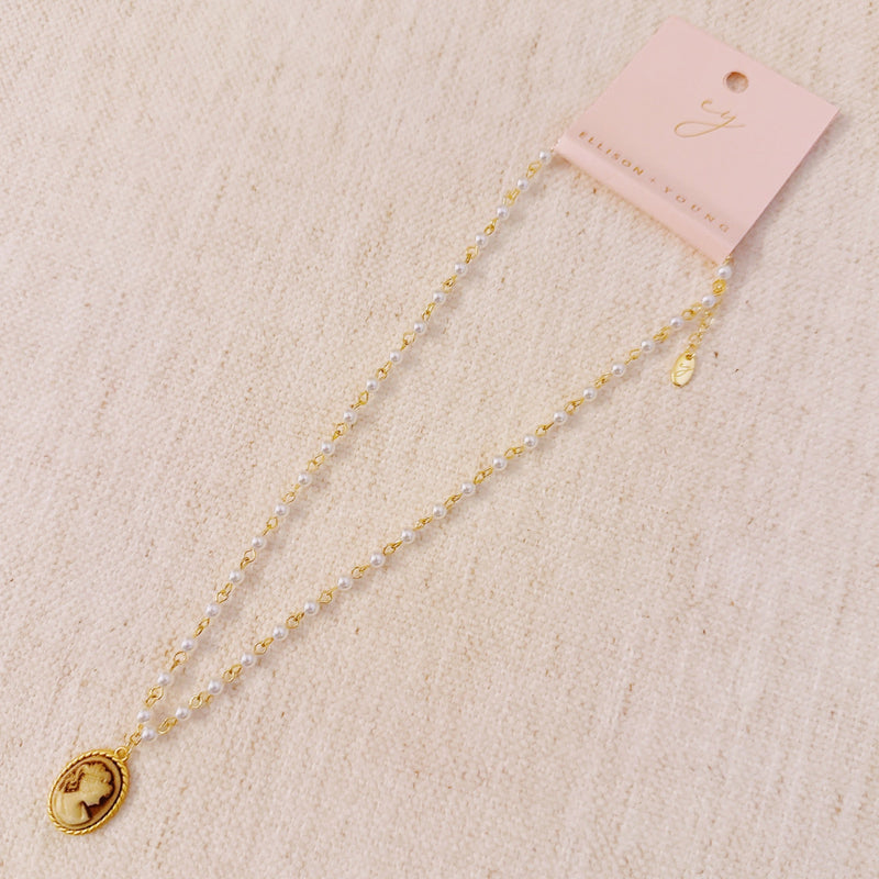Vintage-style necklace featuring a classic cameo pendant framed in gold-tone detailing, suspended from a pearl-accented chain for an elegant and timeless look.