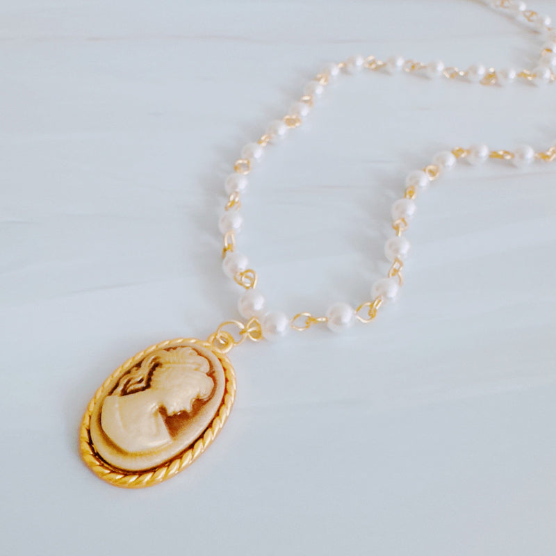 Vintage-style necklace featuring a classic cameo pendant framed in gold-tone detailing, suspended from a pearl-accented chain for an elegant and timeless look.