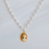 Vintage-style necklace featuring a classic cameo pendant framed in gold-tone detailing, suspended from a pearl-accented chain for an elegant and timeless look.