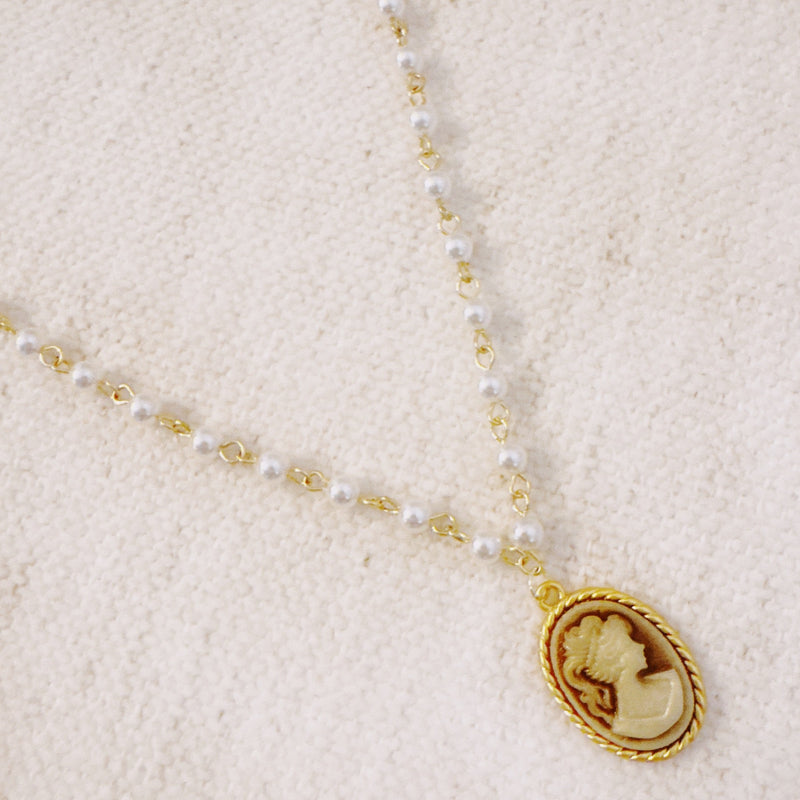 Vintage-style necklace featuring a classic cameo pendant framed in gold-tone detailing, suspended from a pearl-accented chain for an elegant and timeless look.