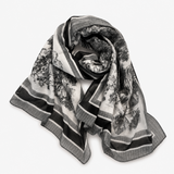 A black and white patterned scarf with stripes and a scenic landscape print, draped on a light gray background.