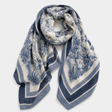A square silk scarf with a blue and off-white toile pattern, featuring a central floral motif and striped borders, displayed on a neutral light gray background.