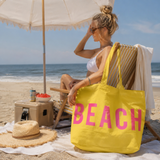 Woman on a beach with a yellow tote bag labeled 'BEACH' and an umbrella.