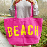 Person holding a pink tote bag with 'BEACH' written in yellow.