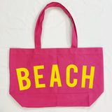 Pink tote bag with 'BEACH' in yellow on a white background
