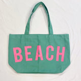 Green tote bag with pink 'BEACH' text on a white background