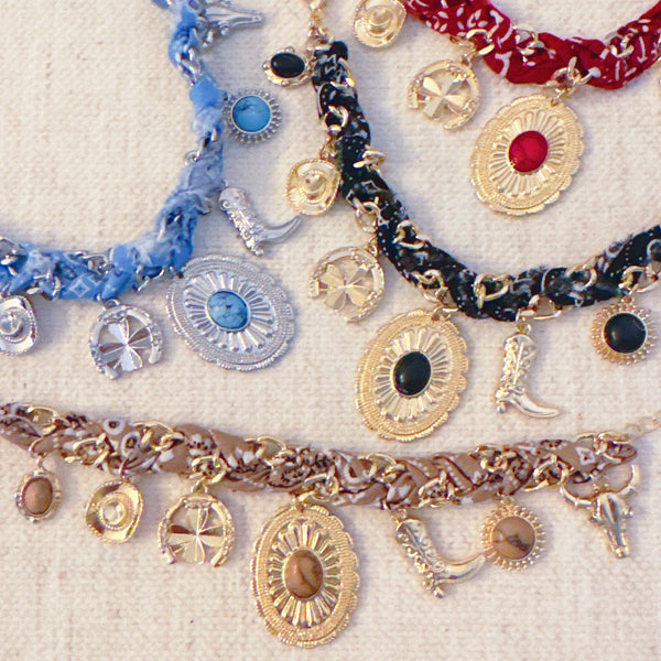 Scarf-wrapped bracelet featuring gold and sliver-tone Western-themed charms including a cowboy boot, sunburst, and lasso motifs