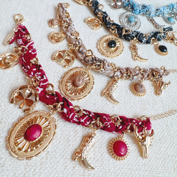 Scarf-wrapped bracelet featuring gold and sliver-tone Western-themed charms including a cowboy boot, sunburst, and lasso motifs
