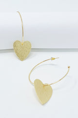 Gold hoop earrings with heart drop charm displayed on white jewelry holder