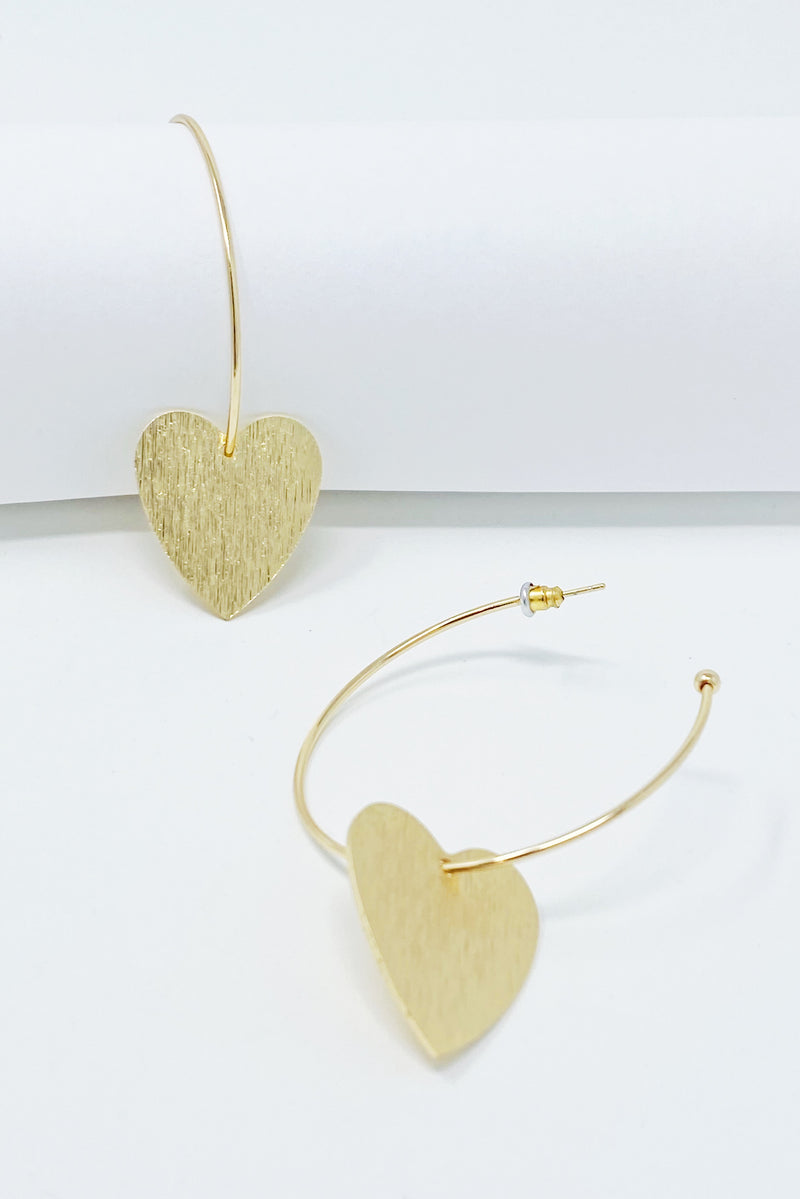 Gold hoop earrings with heart drop charm displayed on white jewelry holder