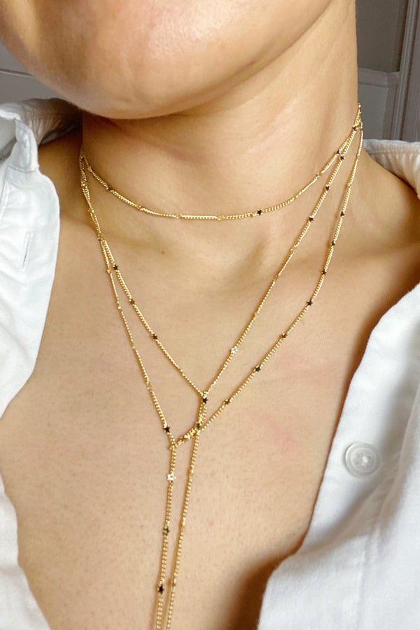 Woman wearing layered gold chain necklace with tiny star charms 
