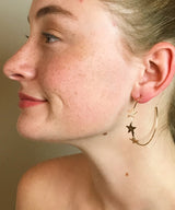 Model wearing gold open hoop earrings with three stars 