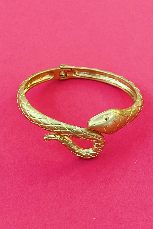 gold snake shape cuff bracelet that open and closes at the head of the snake displayed on pink background