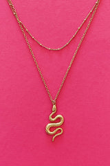 gold double layer necklace with snake pendant displayed on pink background